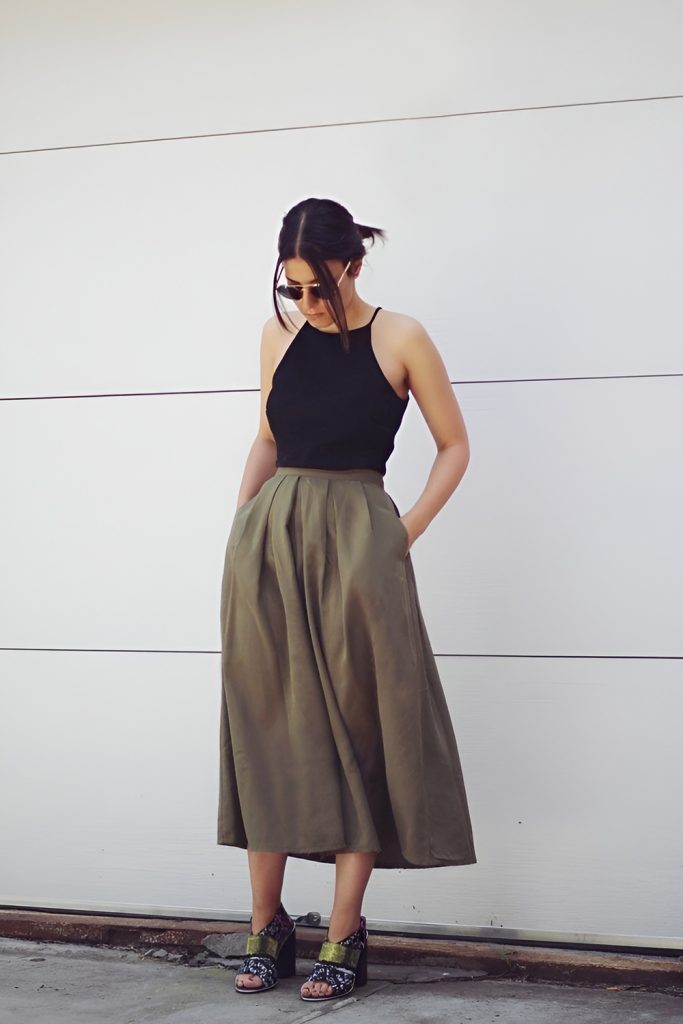 Woman in sunglasses wearing a black halter neck top and an olive green pleated midi skirt with chunky grey green sandals
