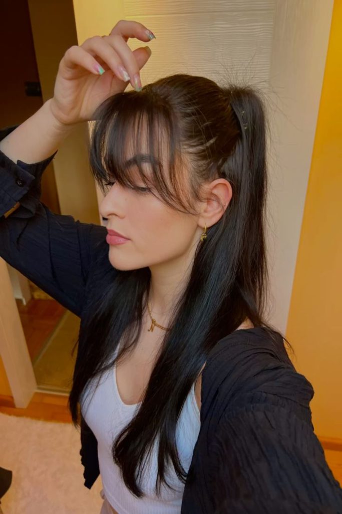 high half up ponytail with long swept bangs and a dark cardigan