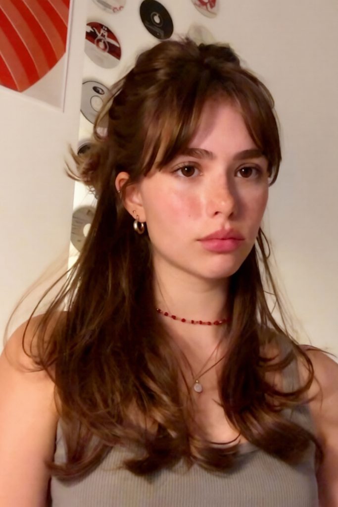 auburn brown half up hairstyle with full bangs and a red bead necklace