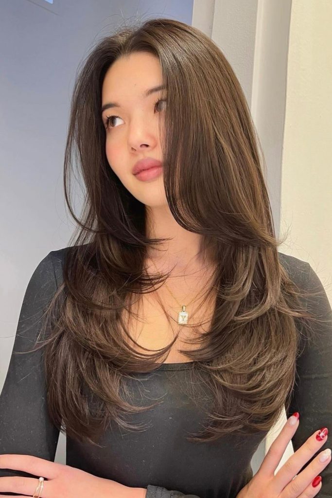 Long dark brown layered hair worn with a black top and red nail polish, looking off to the side