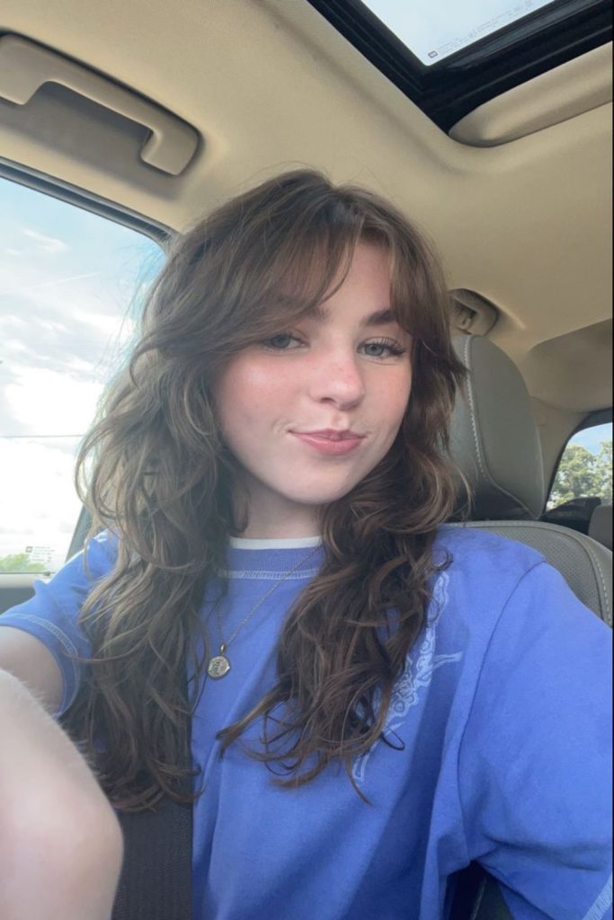 long wavy brown hair with side swept bangs and a blue sweatshirt