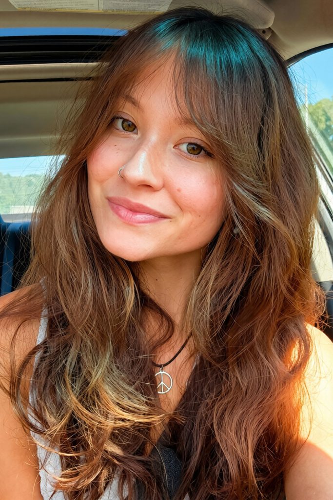 long chestnut brown hair with caramel ends and bangs in a smiling selfie