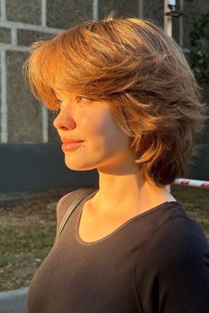 Short shaggy bob with a wispy fringe in a warm copper tone, seen in profile in golden light