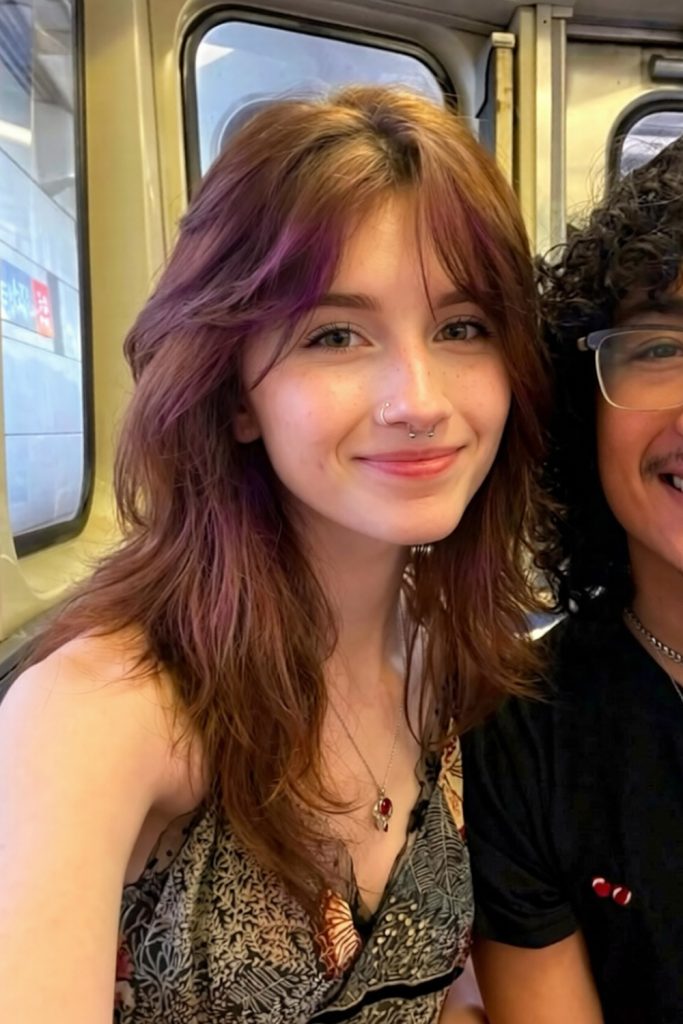 brown layered hair with plum toned streaks and wispy bangs