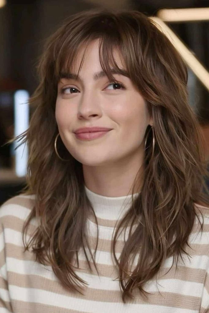 Medium length shaggy brown hair with curtain bangs and hoop earrings, worn with a striped top