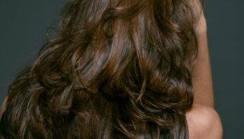 Back view of a woman with long layered tousled brunette hair, kitty cut style