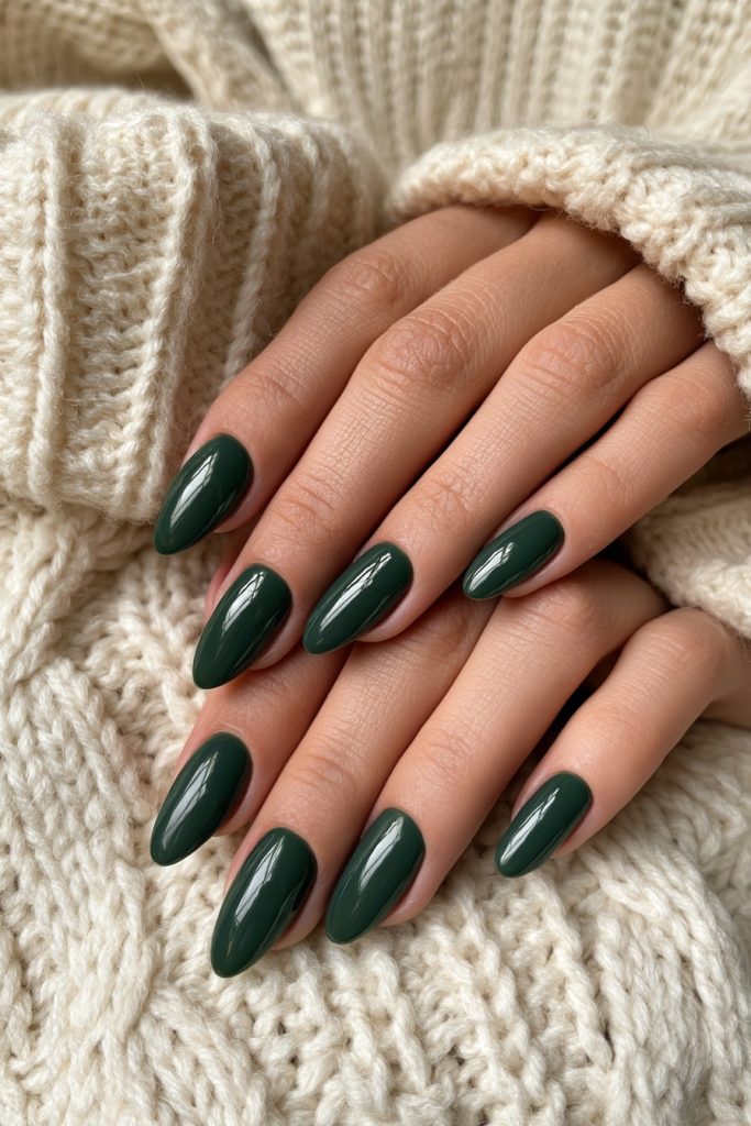 Close up of hands with almond shaped dark green nails resting on a cream knit sweater