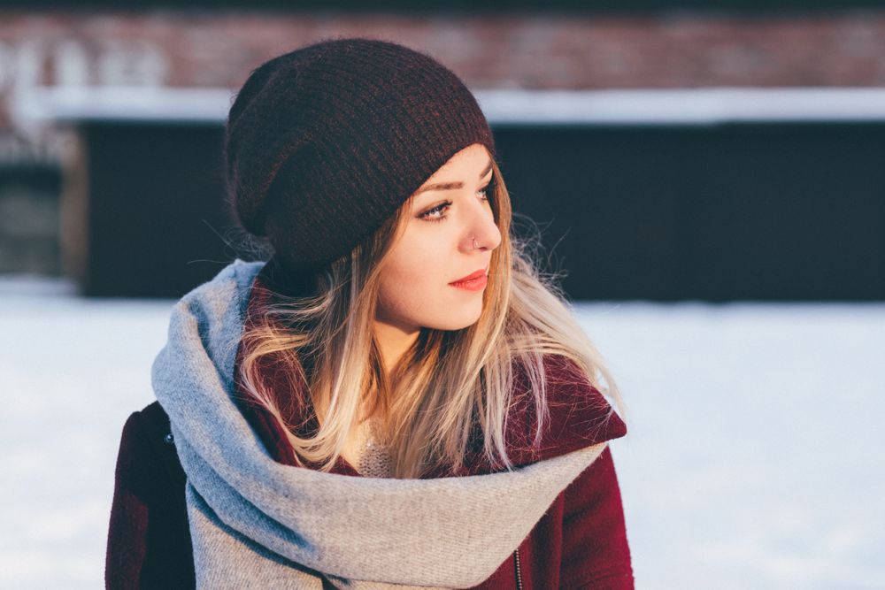 Woman with long blond hair in a black slouchy beanie, a pale grey scarf and a burgundy coat