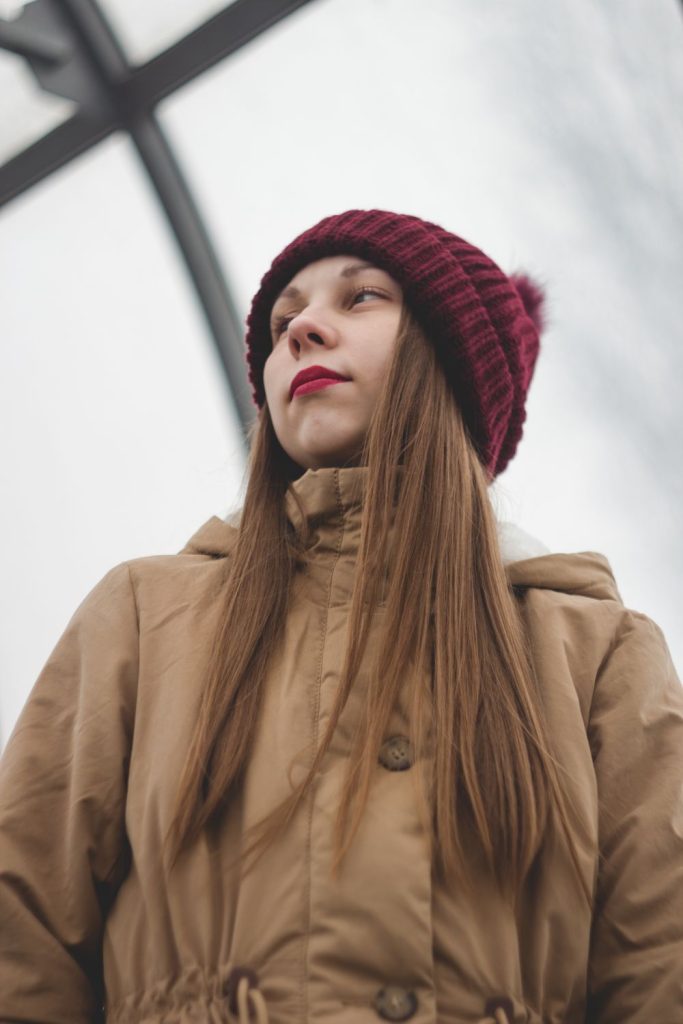Woman with long straight hair in a burgundy pom beanie and a tan hooded coat
