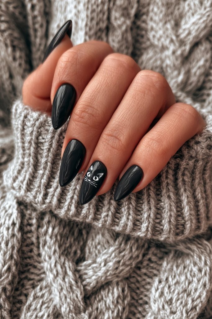 Hand with almond black nails and a tiny white cat face on the ring finger resting on a knit sweater