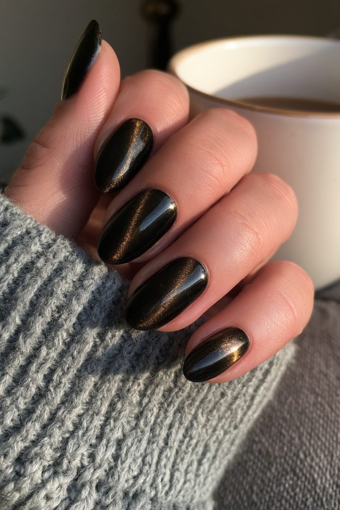 Hand with black velvet cat eye nails and a magnetic gold shimmer holding a coffee cup