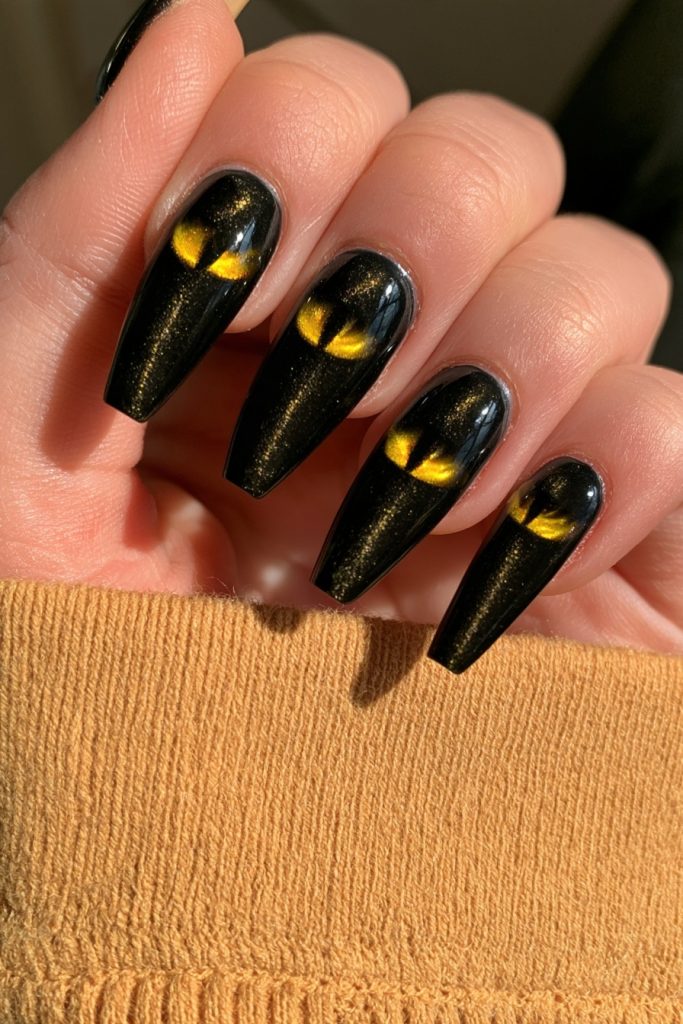 Hand with long coffin black nails with yellow cat eyes on each nail against an orange knit