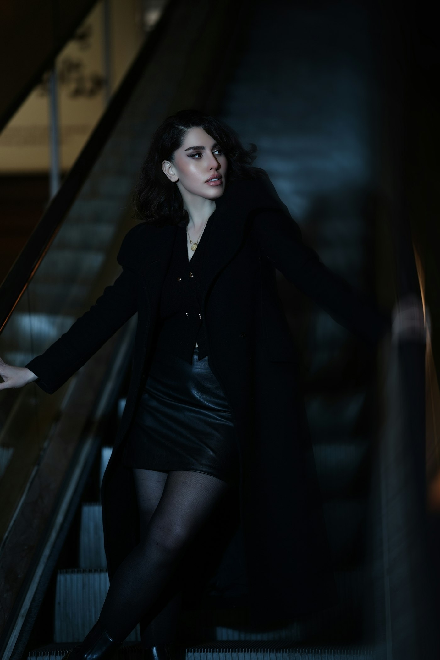 Woman in a black coat and leather skirt on an escalator