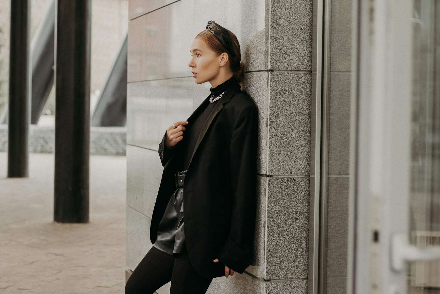 Woman in a black coat and black trousers leaning on a concrete wall
