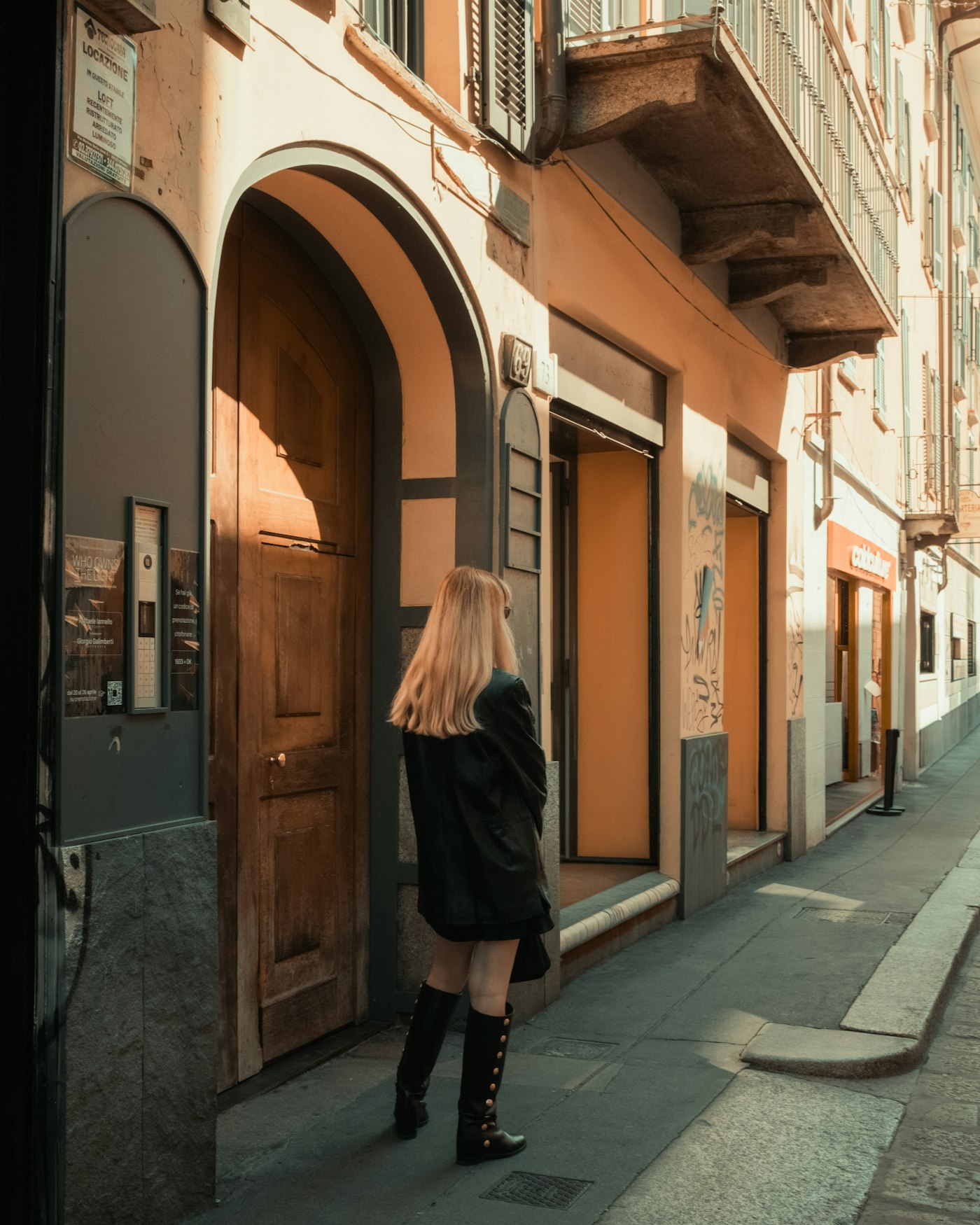 Woman in a black jacket and boots standing by a wooden doorway
