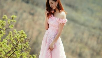 Woman in a pink dress standing near a green tree