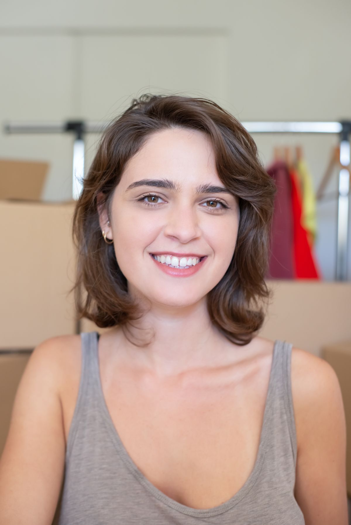 Smiling woman with a wavy chin length bob in warm mid brown, wearing a grey tank top