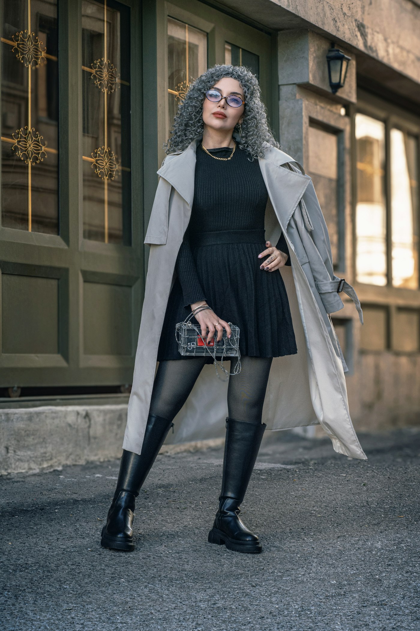 Woman in a trench coat and black dress standing outdoors