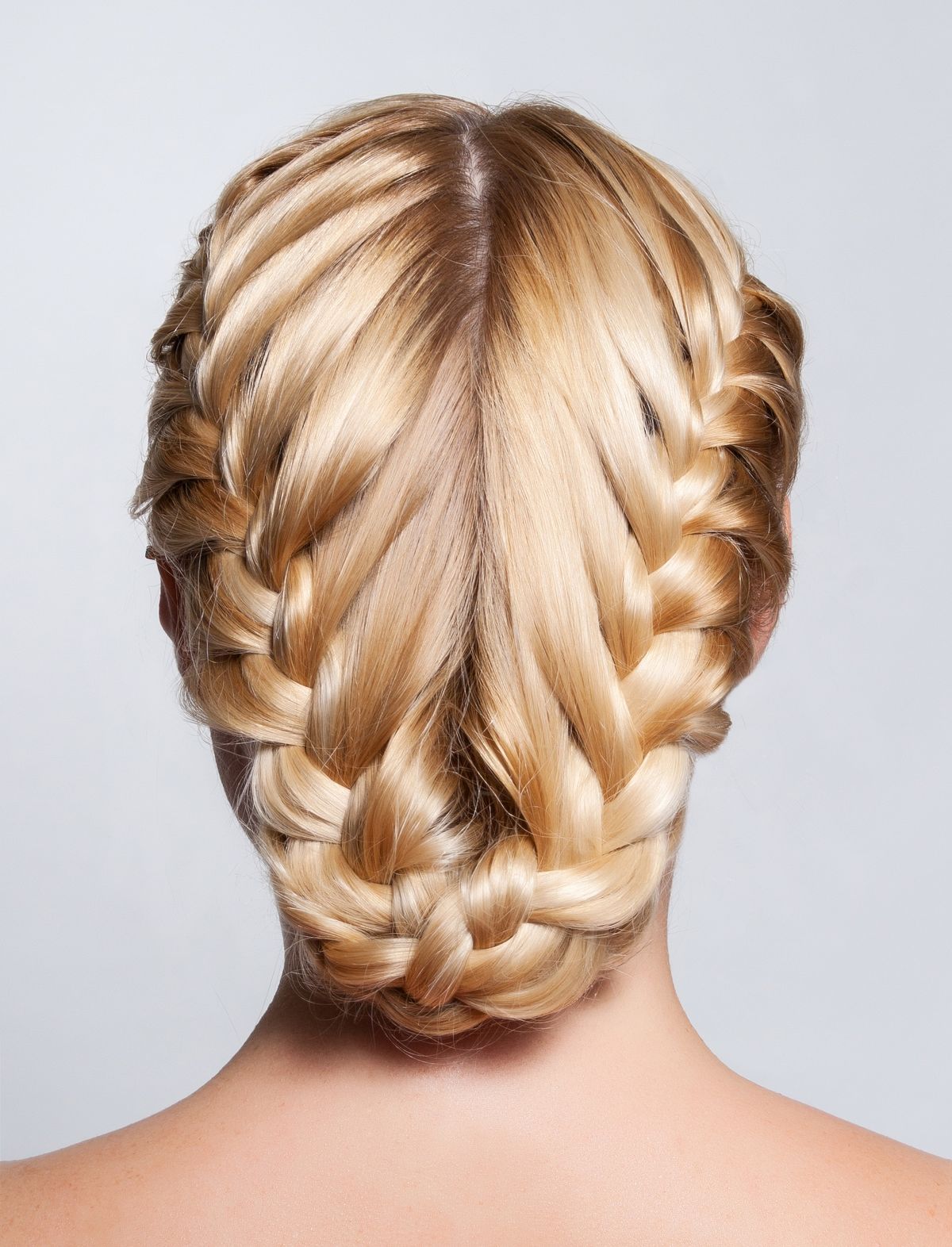 Woman with blonde hair seen from behind wearing two braids that wrap along her head and meet in a braided low bun