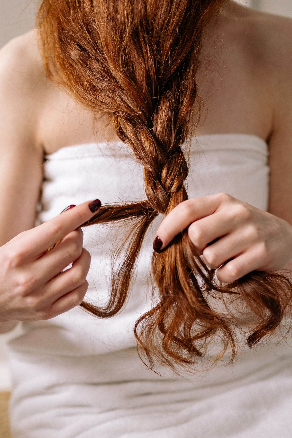 Woman wrapped in a white towel holding a loose auburn three strand braid in both hands