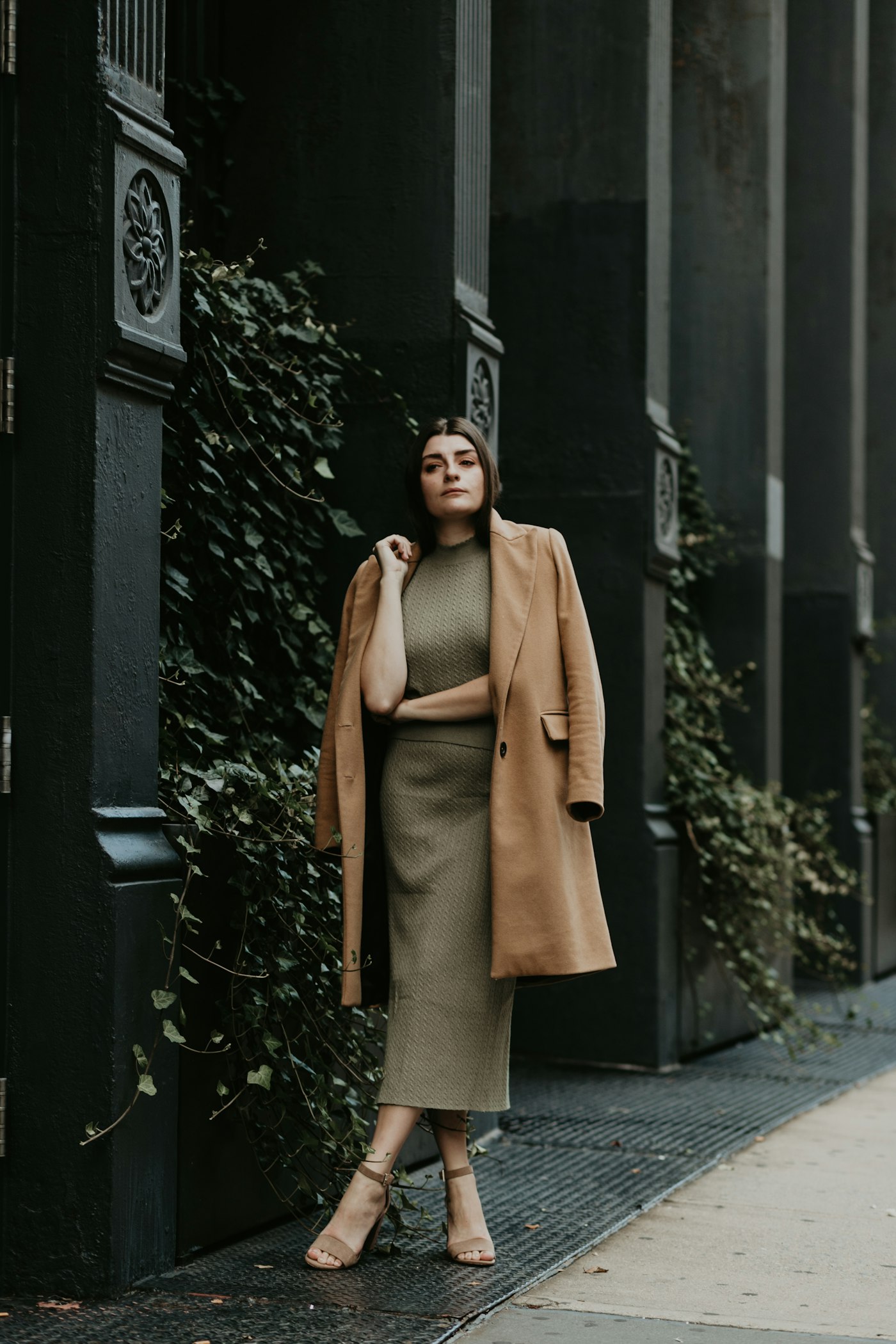 Woman in a brown coat standing near a black metal gate
