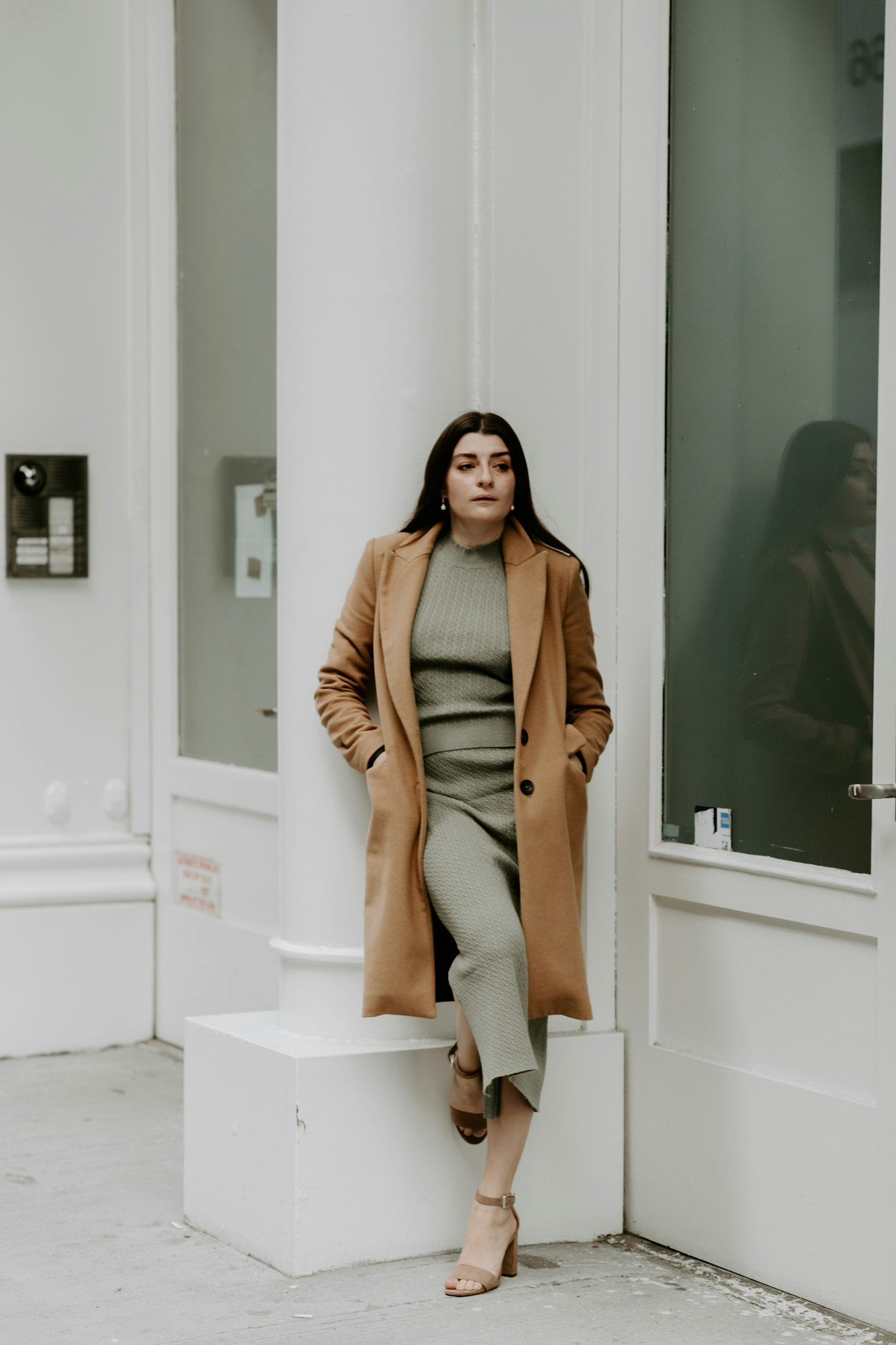Woman in a brown coat and grey trousers on a white staircase