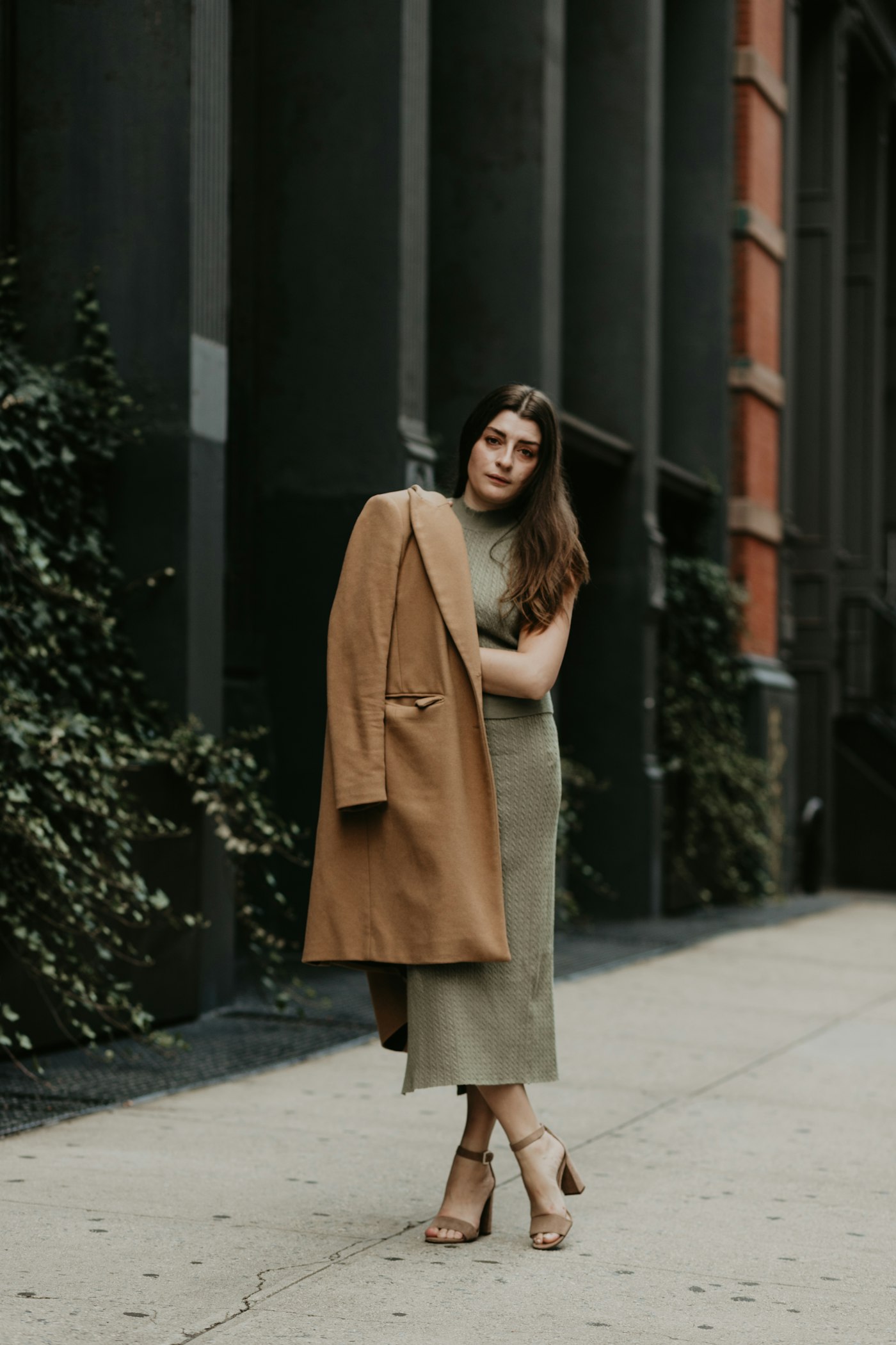 Woman in a brown coat standing on a sidewalk, a coat idea to wear over a dress