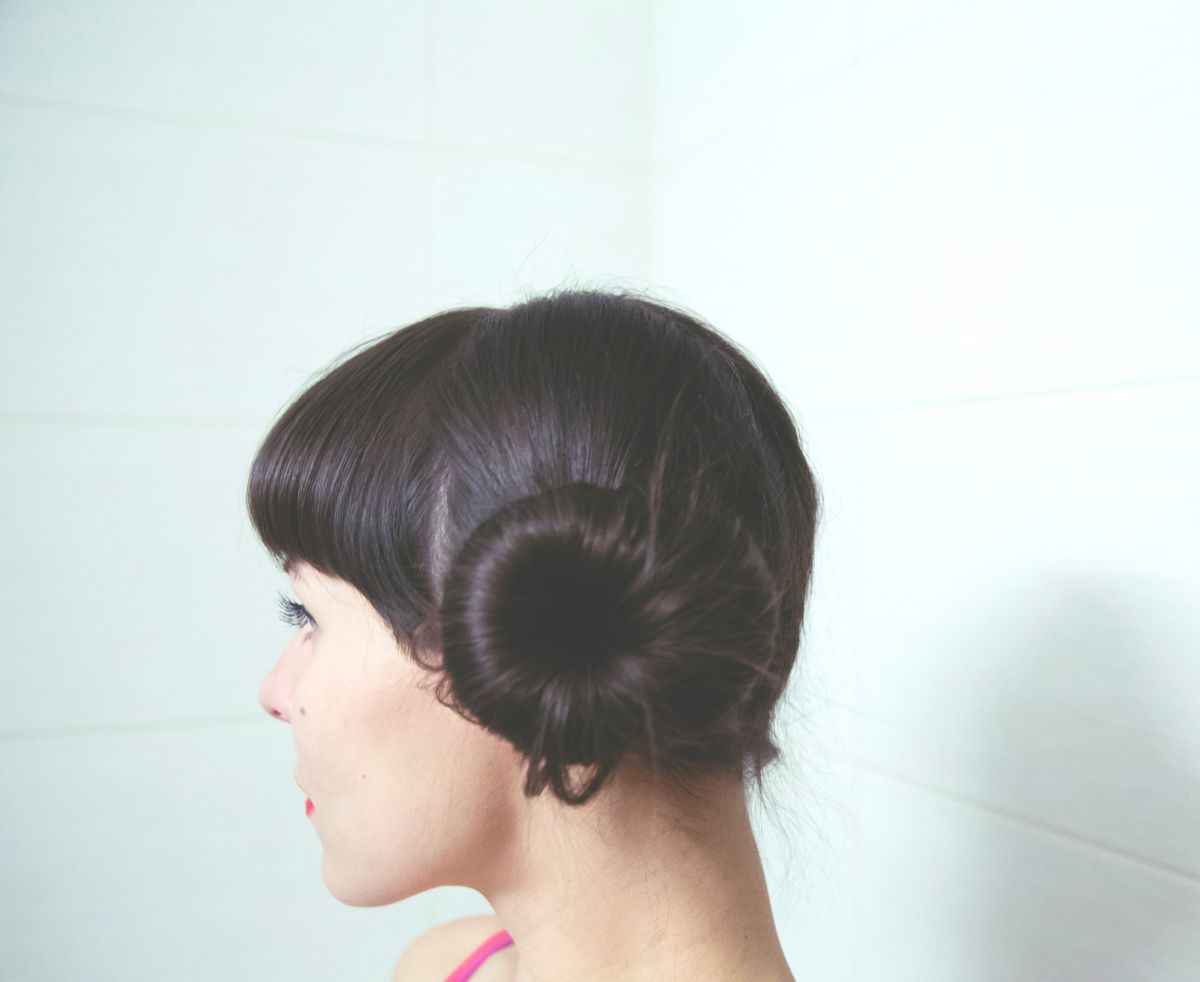 Woman in profile with short dark hair, a blunt fringe and a small coiled bun low at the side of her head