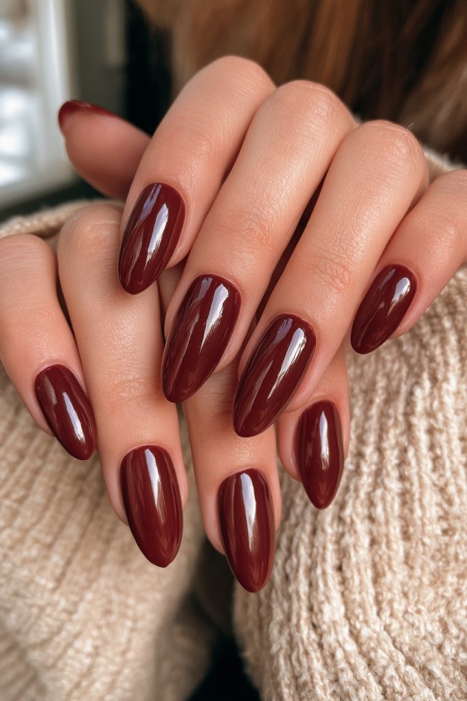 Hands in a cream knit sweater showing long almond nails in glossy deep burgundy polish