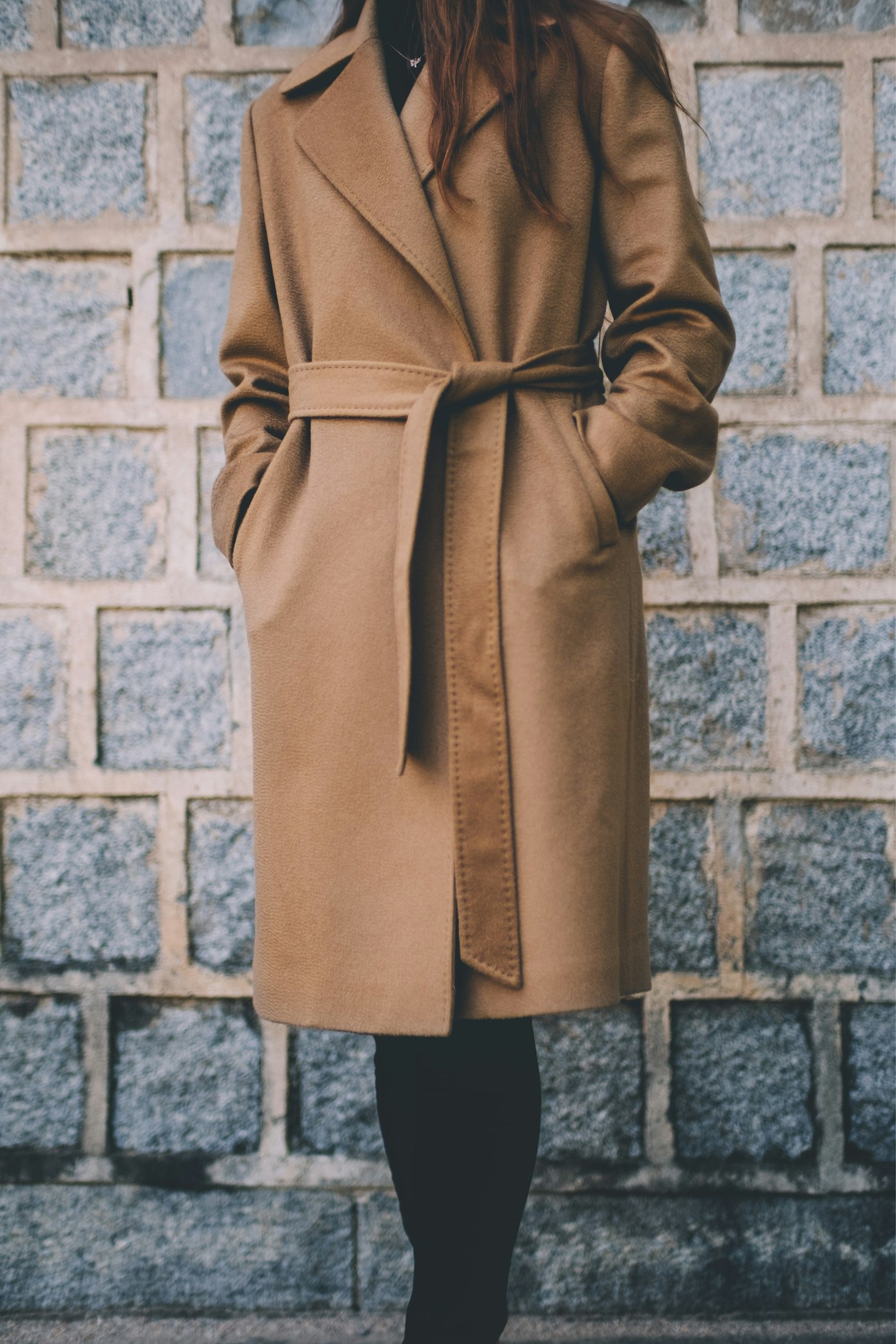 Woman wearing a brown single-breasted coat in front of a grey brick wall