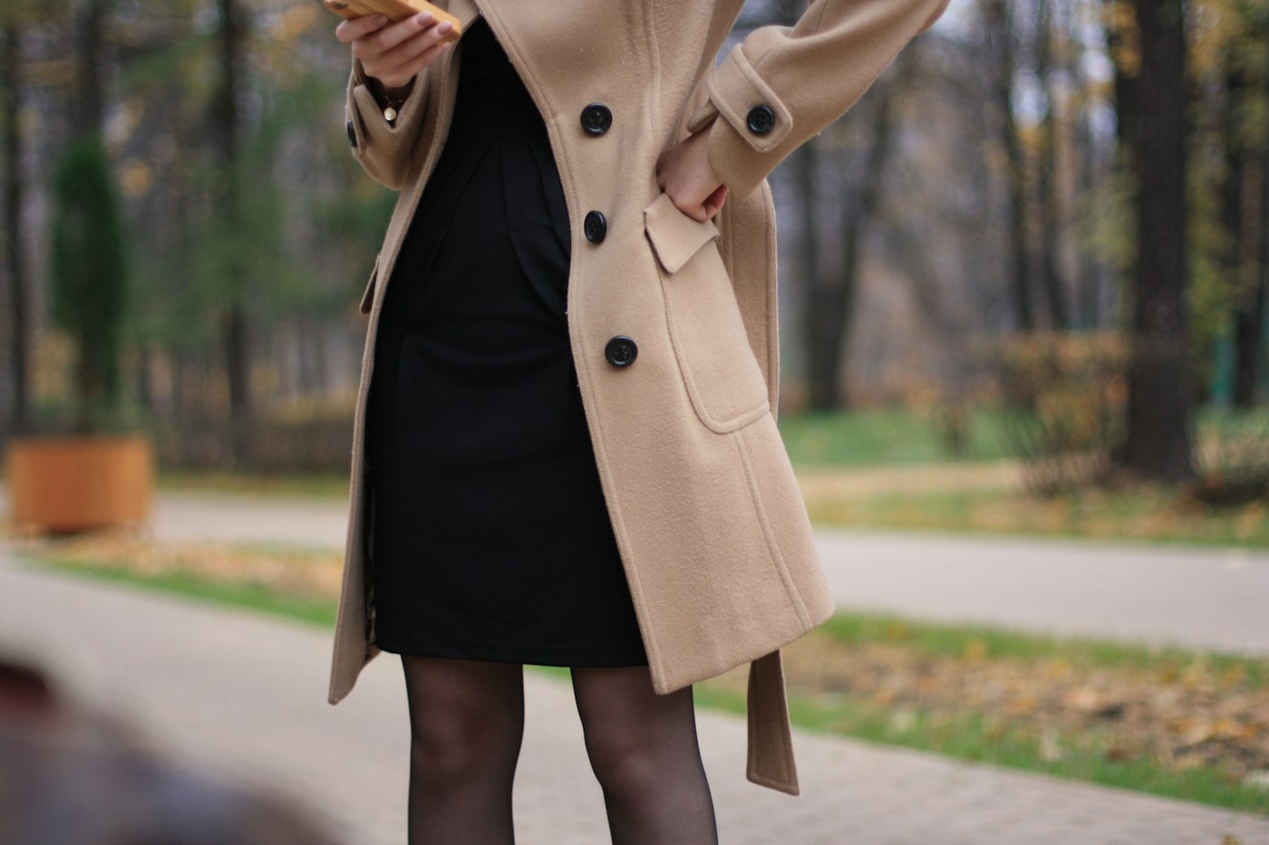 Woman in a brown coat standing on a road in the daytime