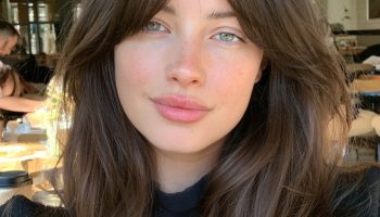 Woman with chestnut brown curtain bangs and long layers in a sunny cafe