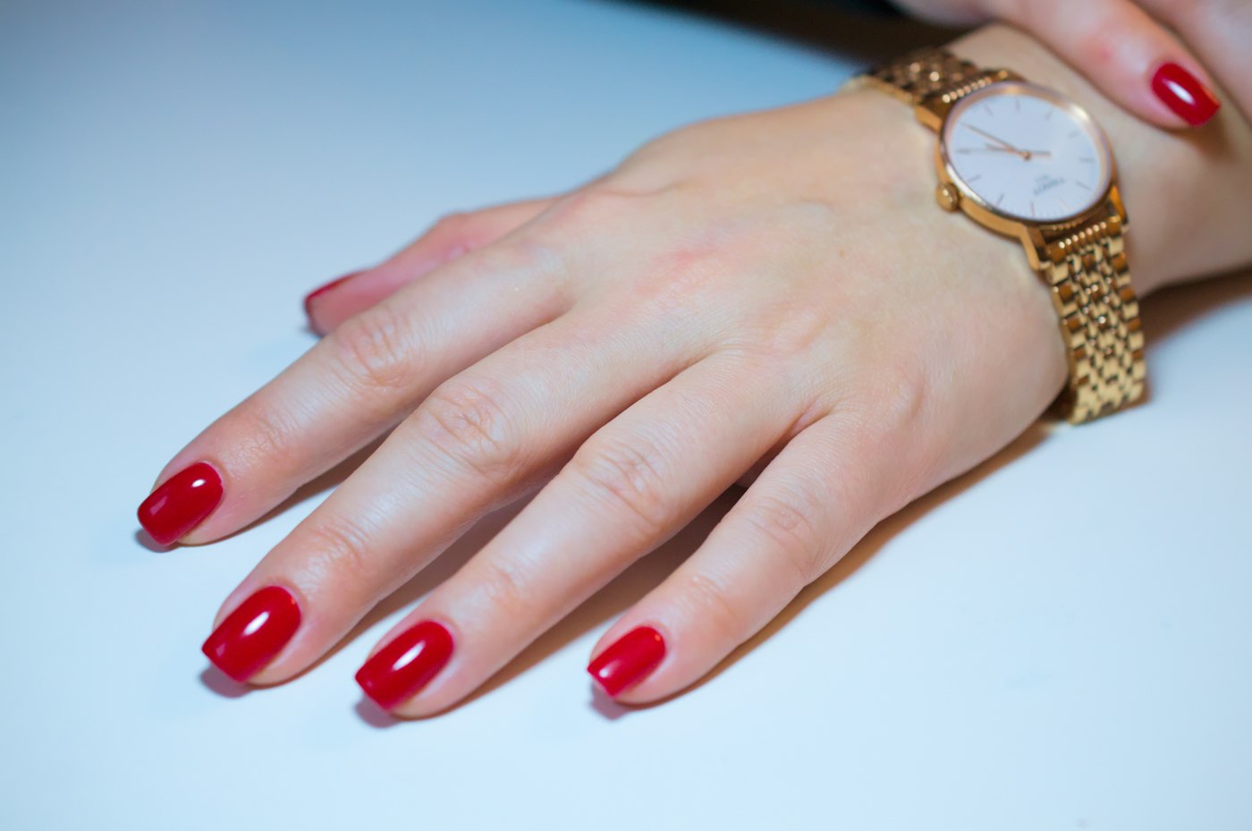 Hand with red painted nails and a gold watch, a classic red Christmas manicure