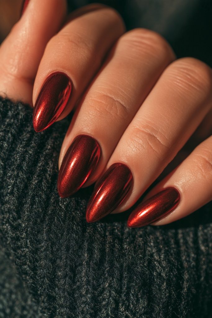 Close-up of a hand with glossy cranberry red almond nails resting on a dark grey-green knit sweater