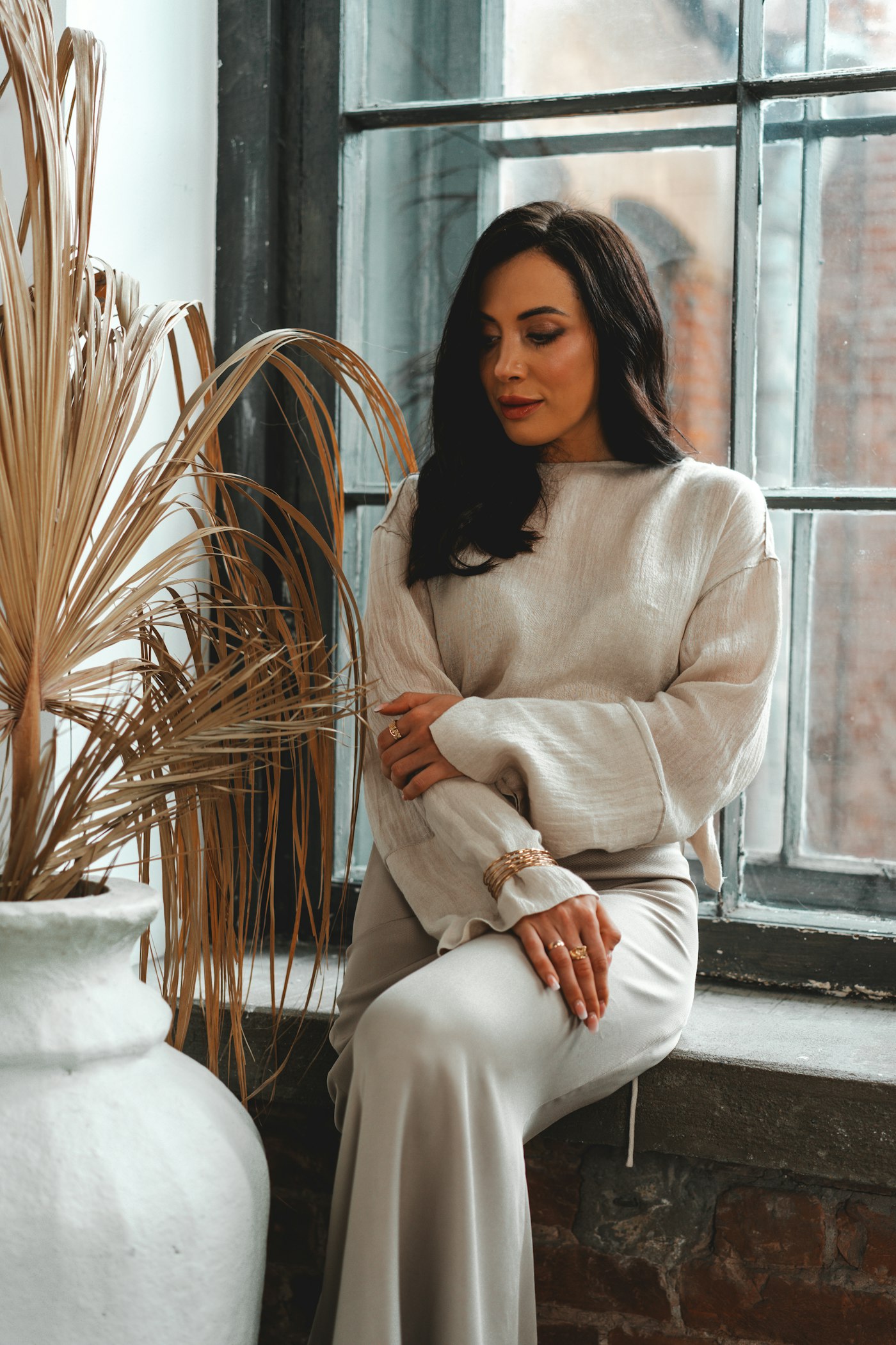 Woman sitting by a window in a cream and beige outfit