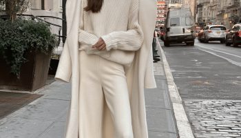 Woman in a cream knit sweater and cream wide leg trousers with a long ivory wool coat worn open on a city street
