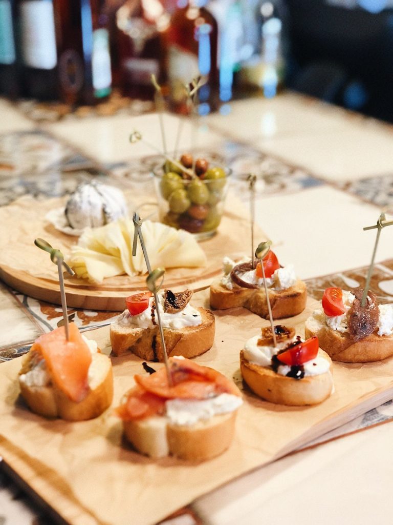 Wooden board of bite-sized crostini topped with cheese, salmon and olives, small appetizers to keep guests satisfied