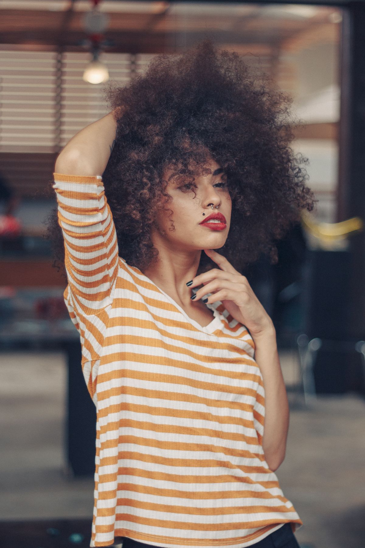 Woman with big dark curls and one arm raised, wearing an orange and white striped t-shirt