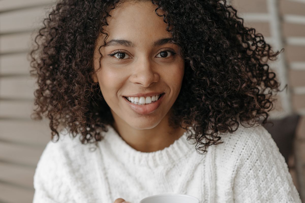 Smiling woman with shoulder length dark curly hair in a white knit sweater