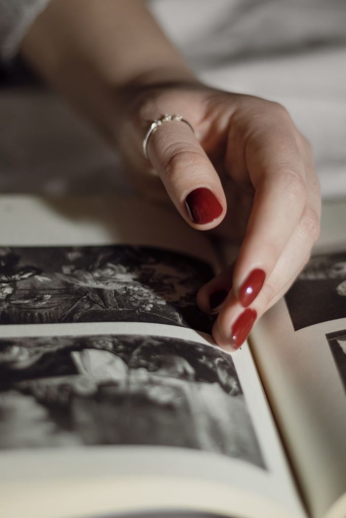 Hand with red nails resting on an open photo book with a ring on one finger