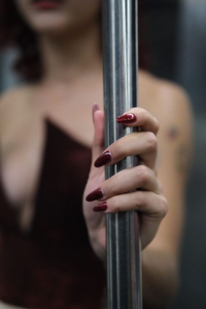 Red nails wrapped around a metal pole with a burgundy top blurred in the background