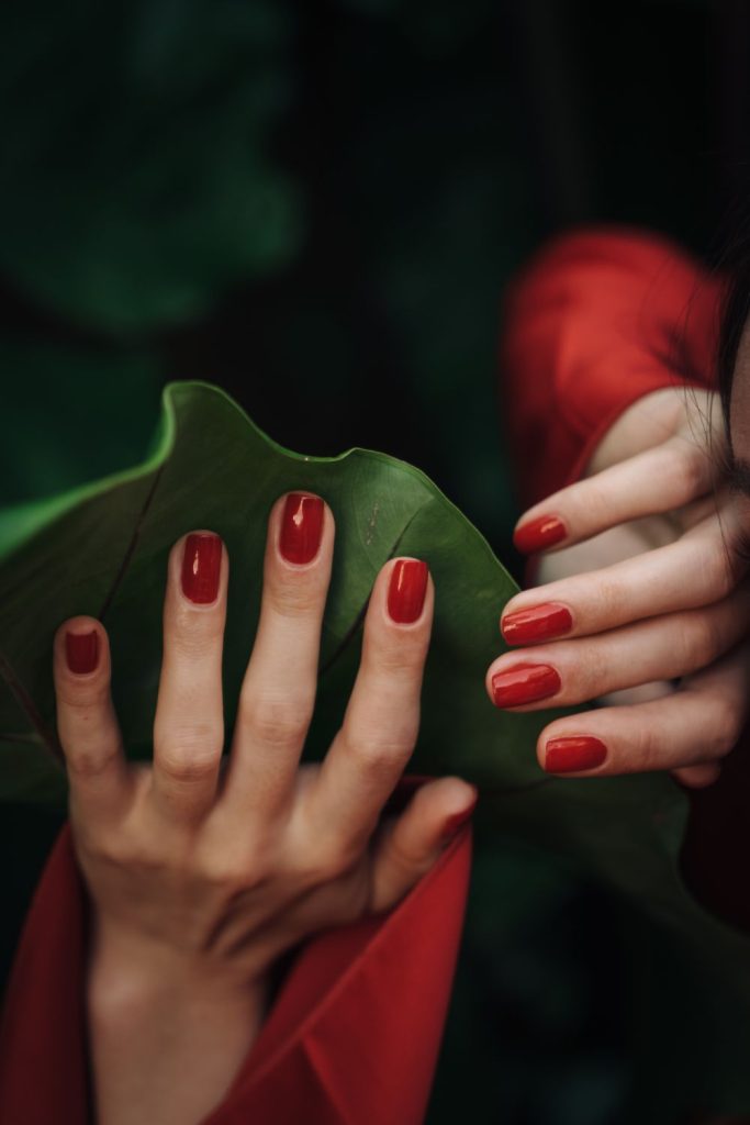 Hand with classic red nails against a large green leaf and a red sleeve