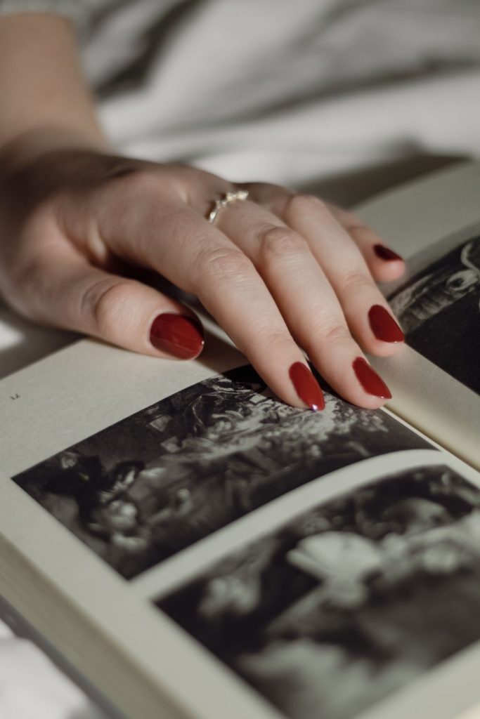 Hand with red nails resting on an open black and white photo book with a ring on one finger