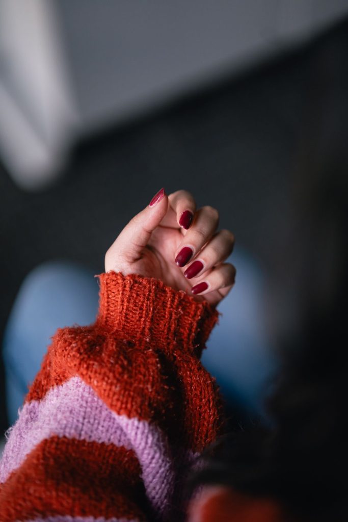 Hand with red nails against a chunky knit sleeve in orange and pink stripes