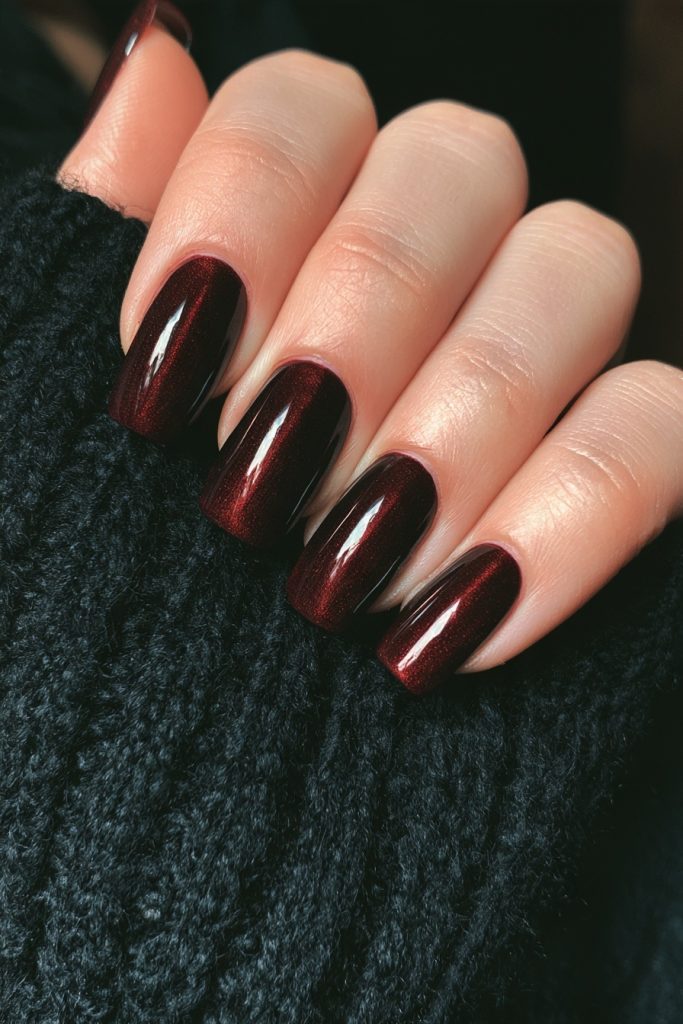 Hand with long almond nails in glossy dark oxblood burgundy resting on a black knit sweater