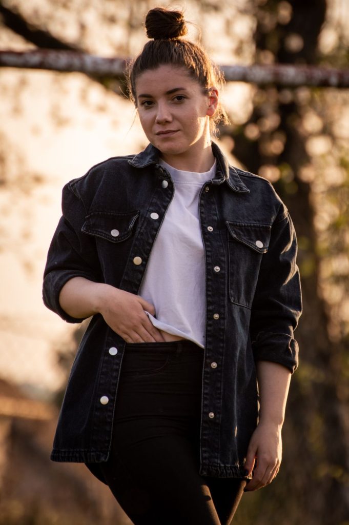 Woman in a black denim jacket, a white tee and a black skirt at golden hour