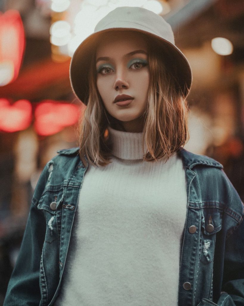 Woman in a cream bucket hat, a grey knit and a dark washed denim jacket with a shoulder-length bob