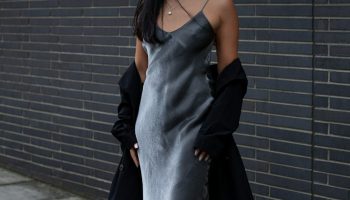 Metallic silver slip dress with a black coat against a brick wall