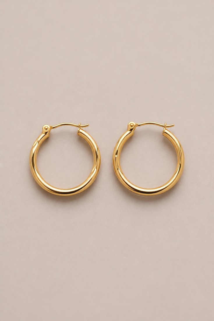 A pair of small polished gold hoop earrings on a soft grey backdrop