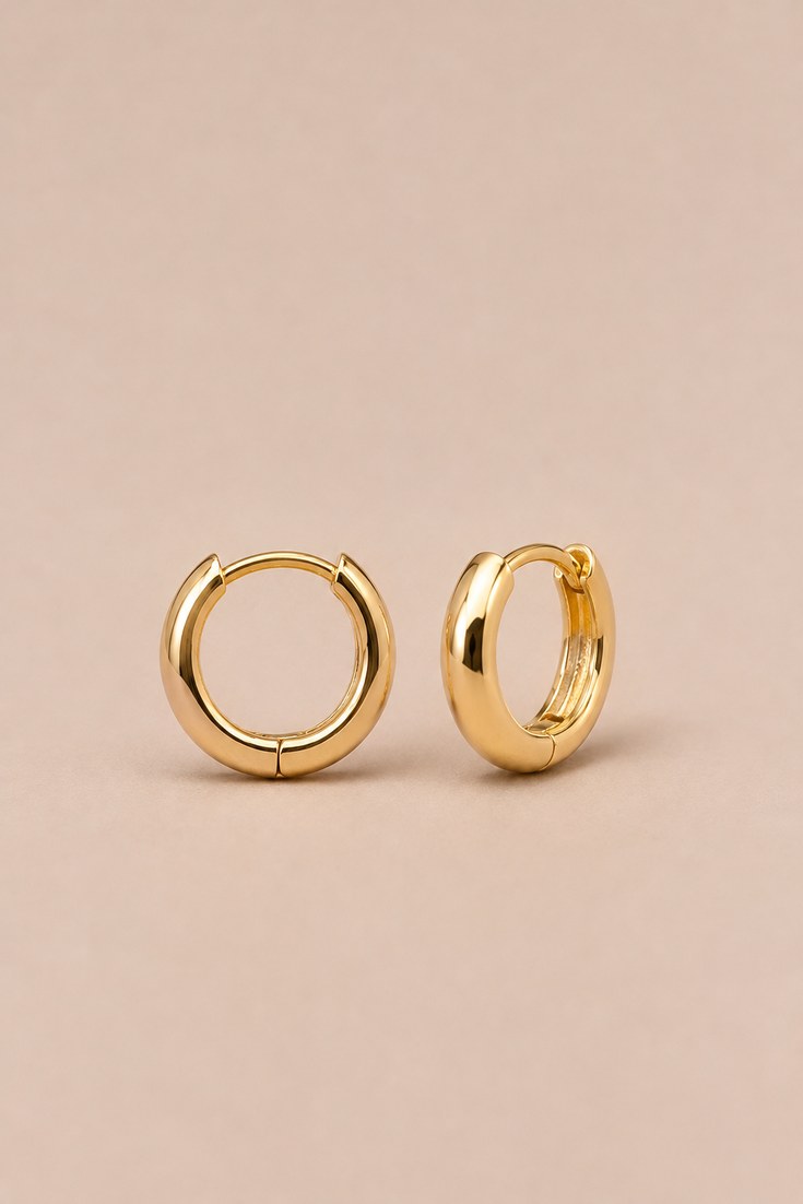A pair of small gold huggie hoop earrings with a tiny pave sparkle on a beige backdrop